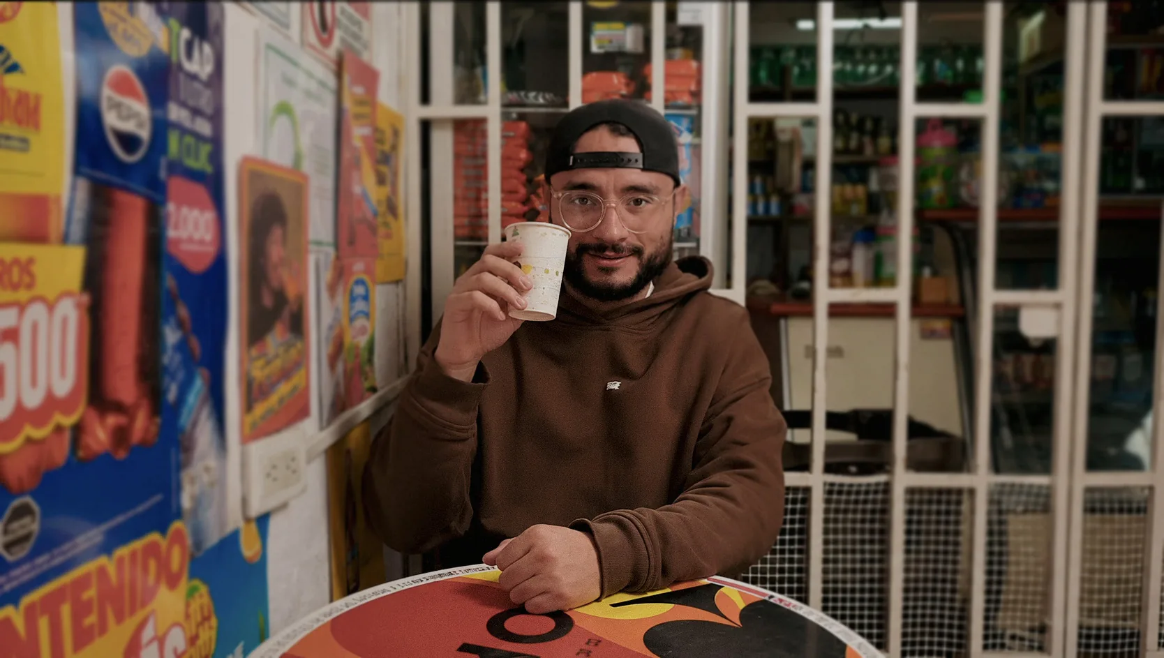 Chimuelo tomando tinto frente a la reja de una tienda de barrio