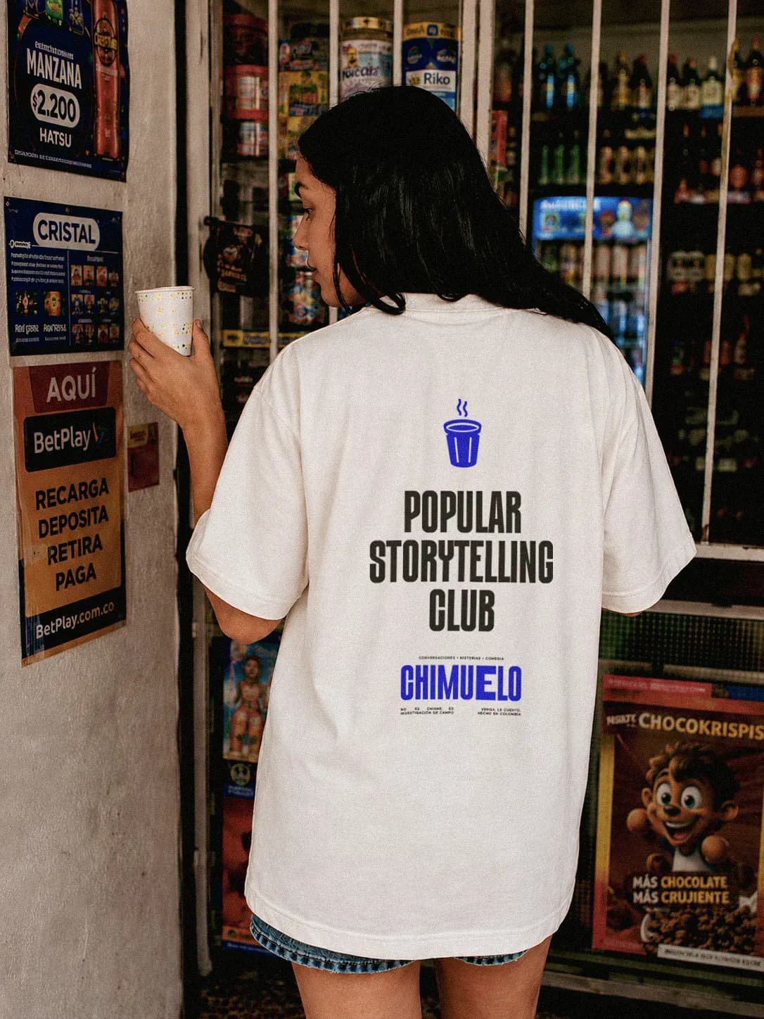 Persona de espaldas en una tienda con la camiseta blanca Popular Storytelling Club de Chimuelo